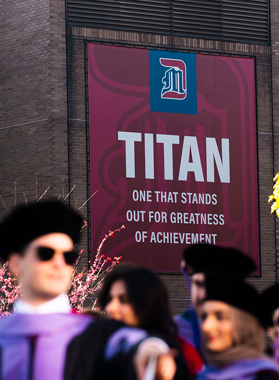 Graduates line up near the Titan sign that reads "one that stands out for greatness of achievement."
