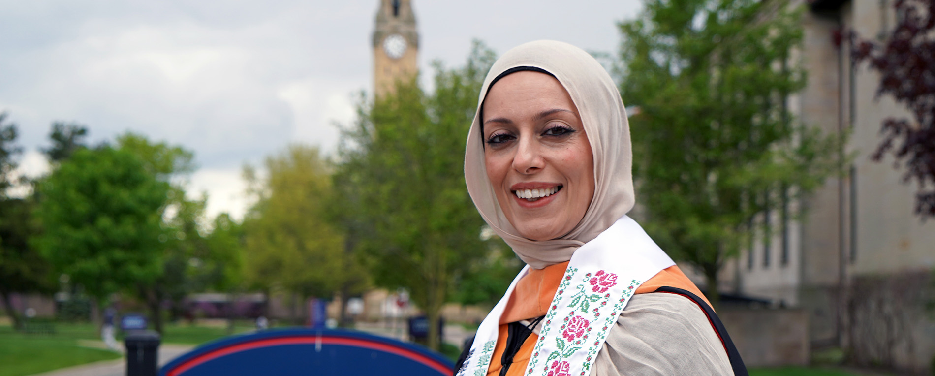 Shreen Marini stands outside the Health Professions Building at UDM with the clocktower in the background.