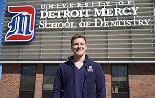 Mack Powell stands in front of the Detroit Mercy School of Dentistry sign.