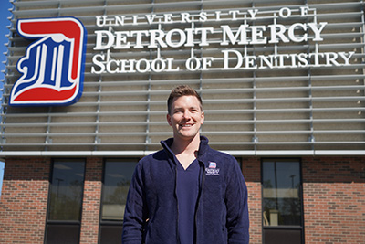 Mack Powell stands in front of the Detroit Mercy School of Dentistry sign.