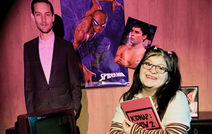 A student actress poses in front of photos of Tobey Maguire which are placed on the wall behind her.