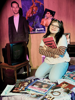 A student actress poses on a bed surrounded by photos of Tobey Maguire.