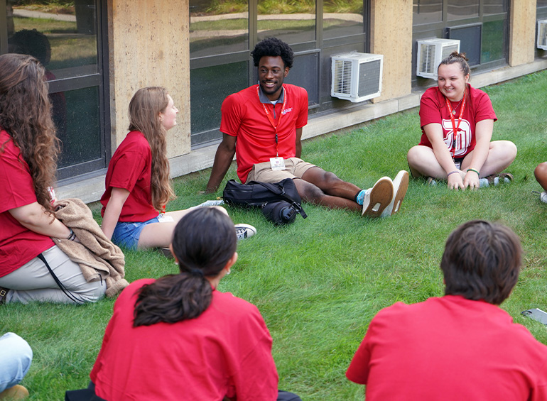 Students gather around each other in the grass during an orientation activity.