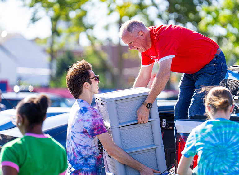 A student helps a man lift something out of a vehicle during move-in day.