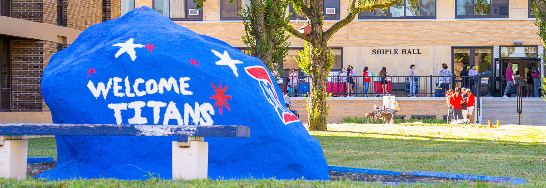 The rock is painted with the message "welcome Titans" while in the background, students are seen moving into Shiple Hall.