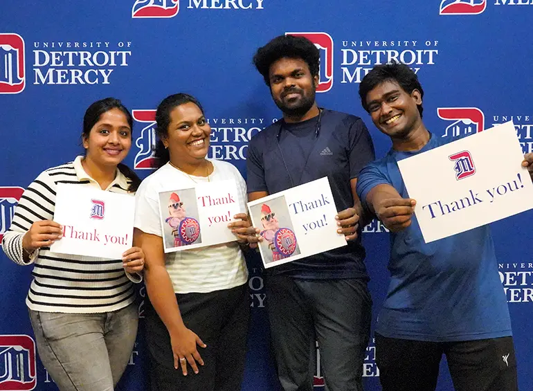 4 students in front of our logo wall holding signs that say thank you