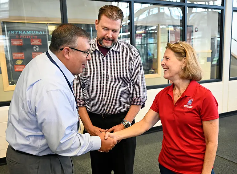 staff member shaking hands with a dean of a school while the man introducing them looks on.