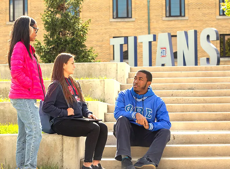 3 students sitting in front of titans sign