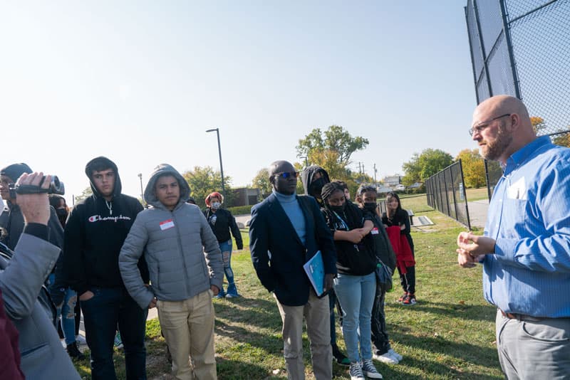 Bioneers Conference event showing high school students outside listening to Nick Schroeck speaking at a stop during the Environmental Justice tour