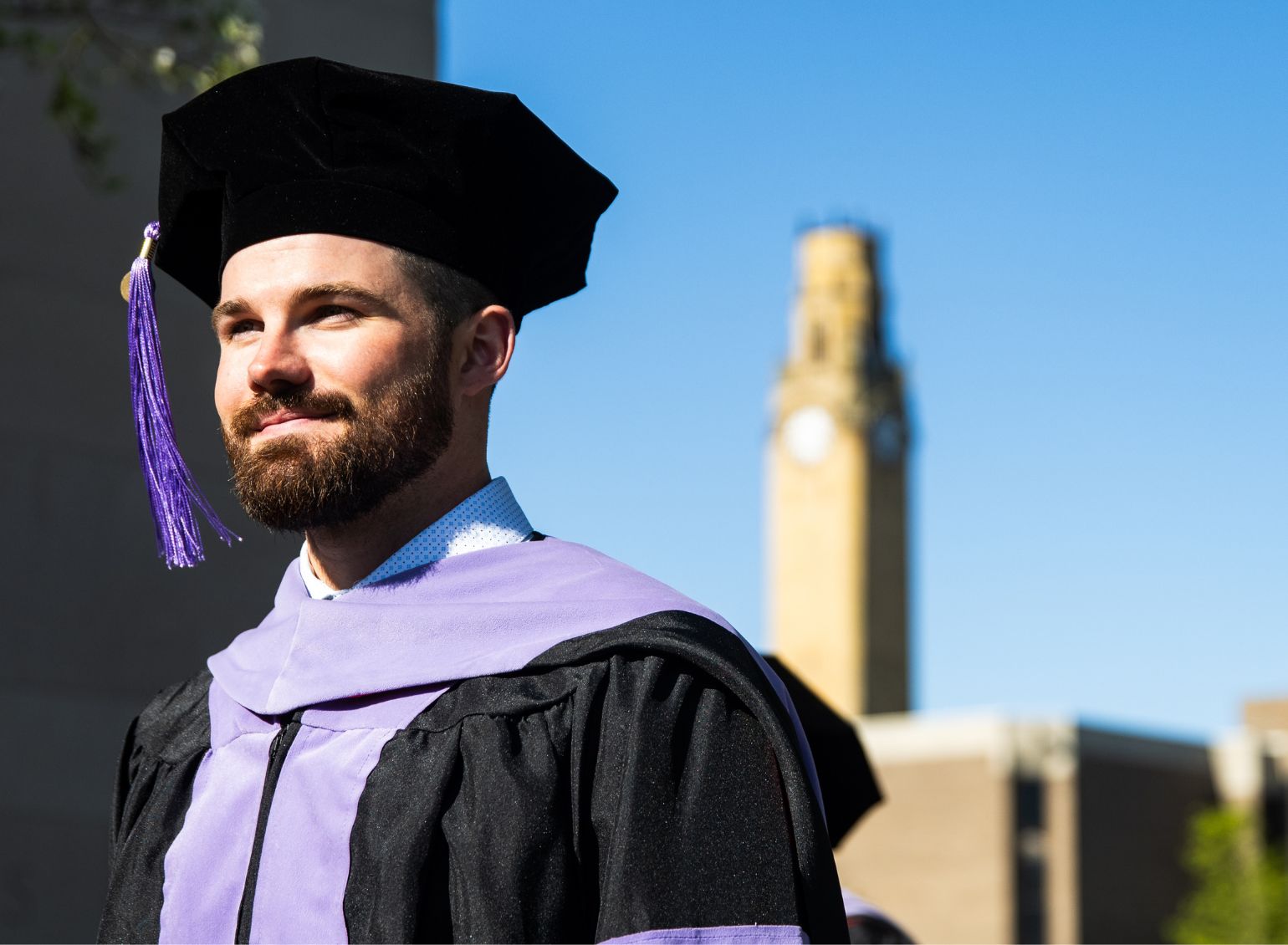 A graduate student stands outside at commencement.