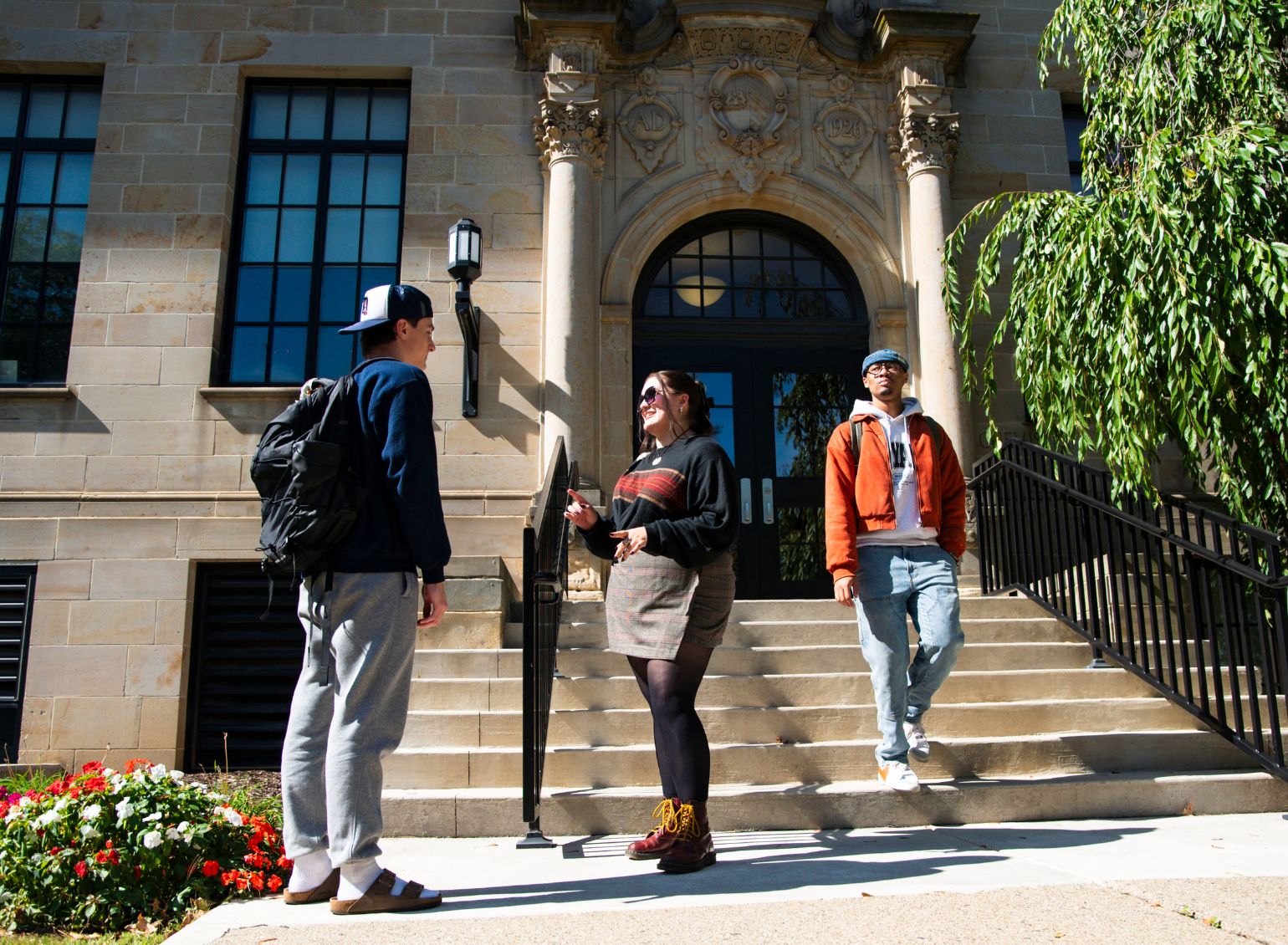 Two students talk while another student walks out of a building.
