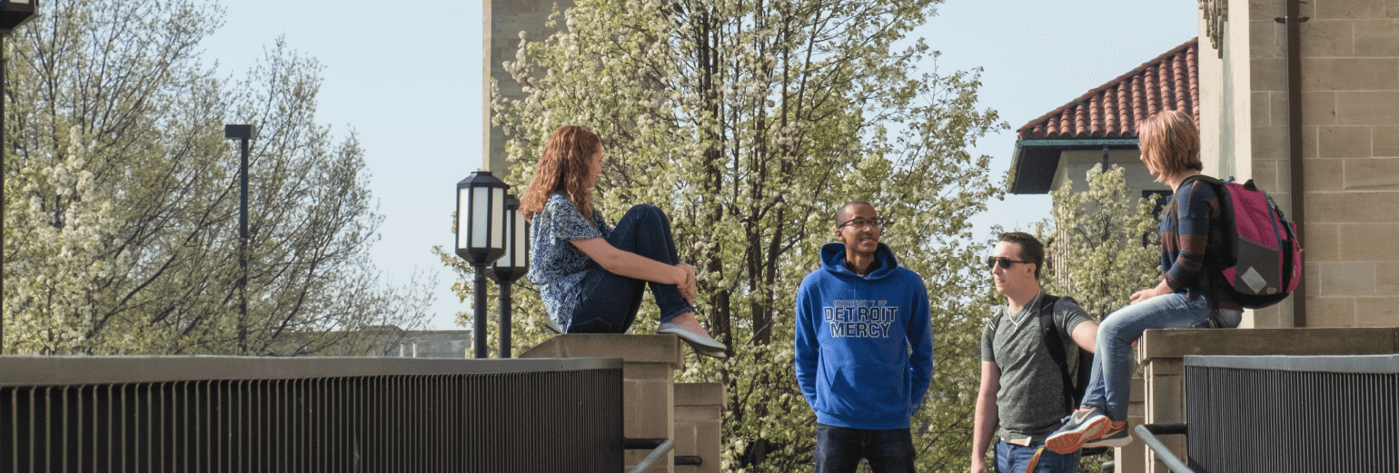 close up of three students sitting outside among a group of students