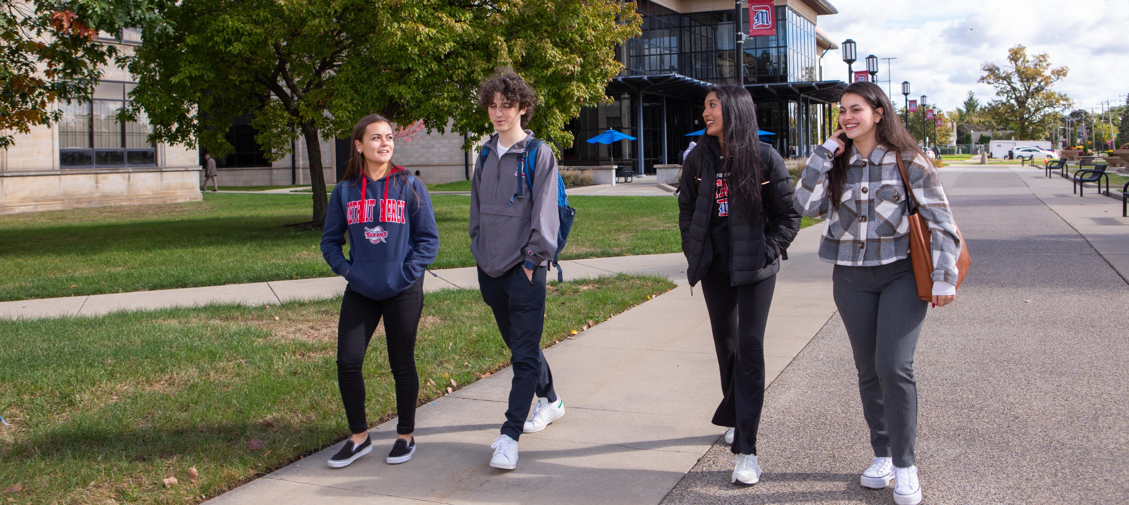 Four UDM students walk on campus during a spring day.