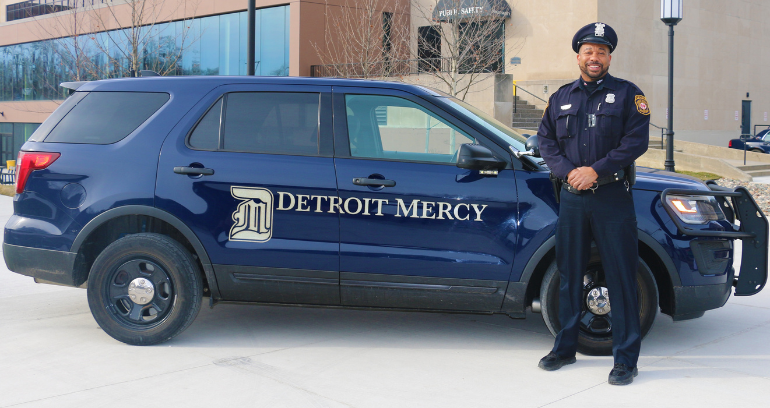 A Public Safety officer stands by a police car.