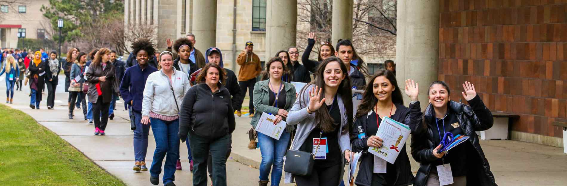 Students walking on campus with their families waving to the camera