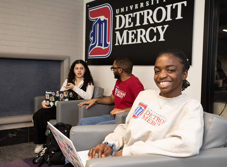 Three students sit in the Student Union, with one looking at the camera smiling.
