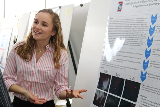 Student explaining her research board at Celebration of Scholarly Achievement