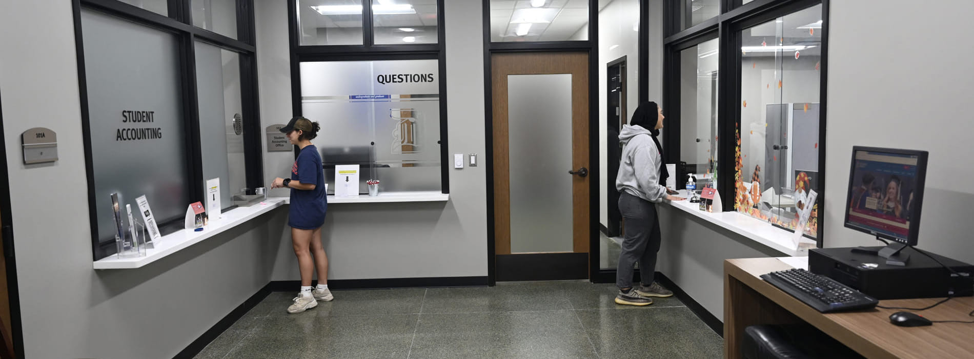 Two students stand near windows inside of the Student Accounting Office in the Student Union.
