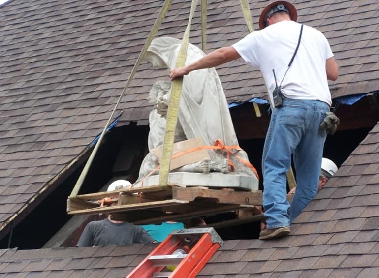 Pieta statue being lifted out of roof with man
