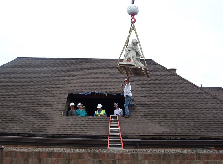 Pieta statue being lifted out of roof with ladder
