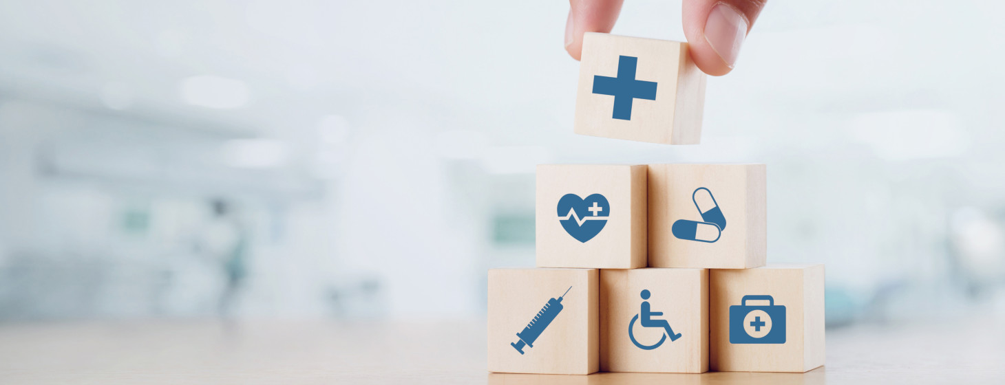 Small tower of wooden blocks with health-related icons on them, with fingers placing a final block on top