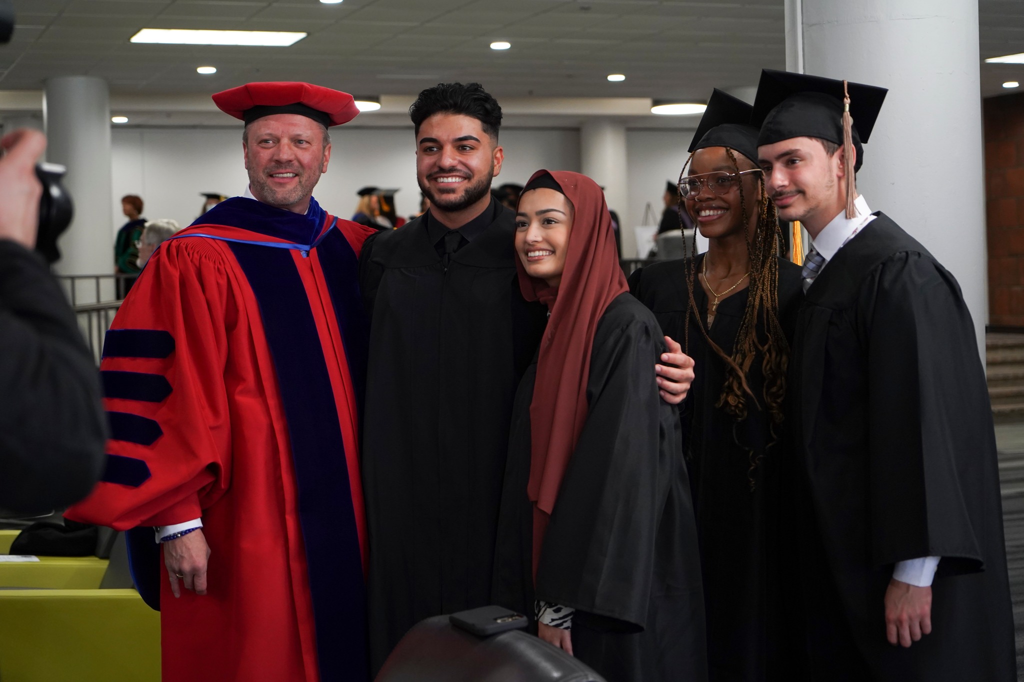 Five people standing inside of the Student Union, pose for a photo, smiling.