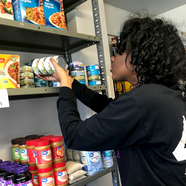 The Hive Operations Coordinator stacks shelves with canned goods.