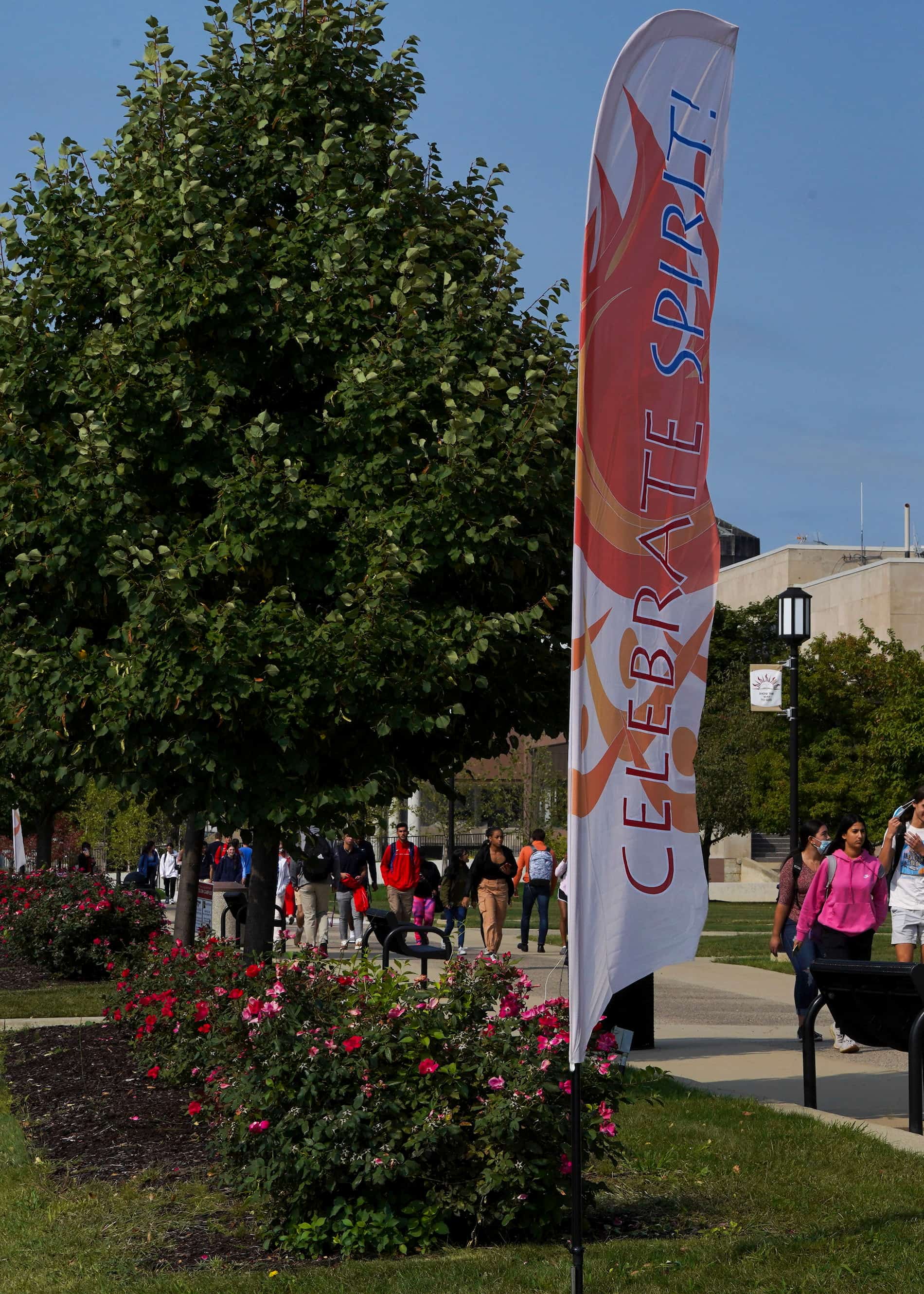 An outdoor shot of a Celebrate Spirit banner with students, trees and a sunny day beyond.