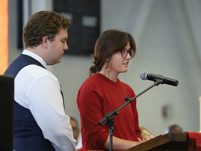 Two students stand and speak from a podium inside of the Student Fitness Center.