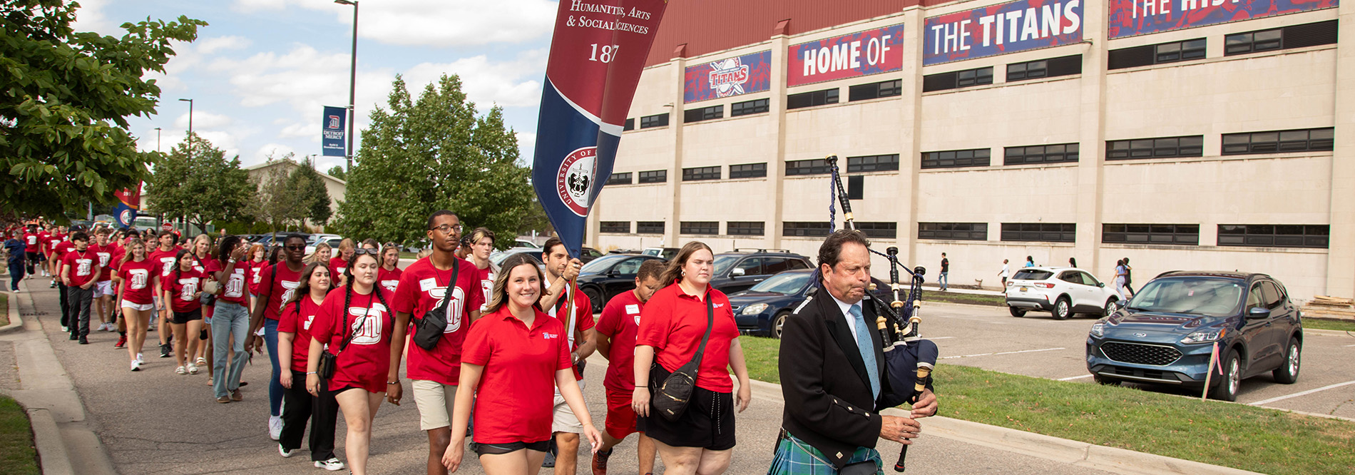 Students walk down the road on the McNichols Campus to first-year convocation, led by a bagpiper.
