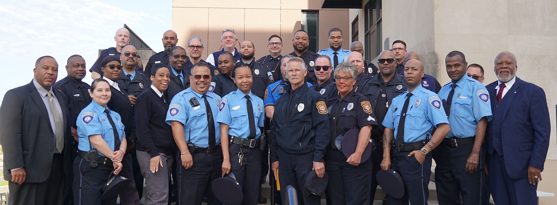 More than two dozen people stand in uniform outdoors in front of the Public Safety entrance.