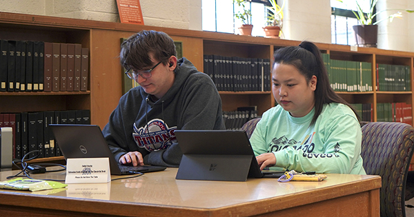 two students on their laptops in the library