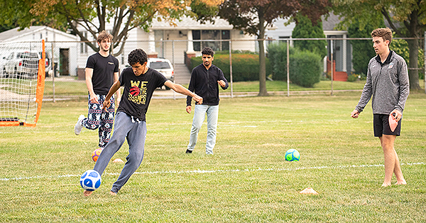 students outside playing soccer with student about to kick the ball