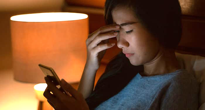 student looking at phone with concerned expression and touching forhead like she has a headache.